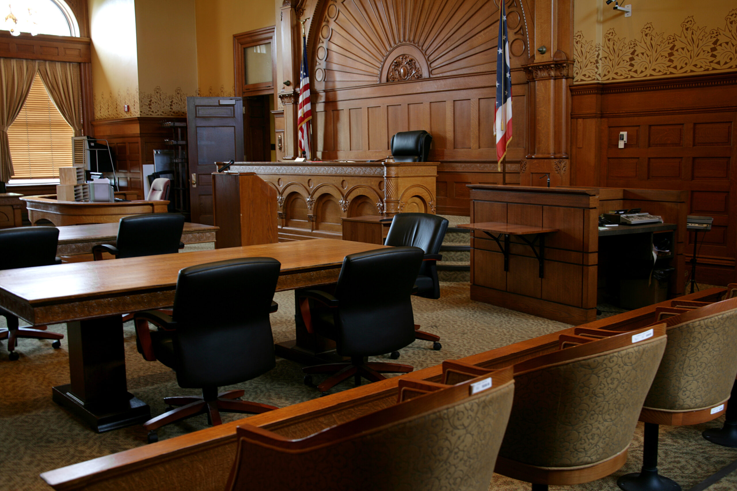 Empty courtroom with wooden furniture and flags.