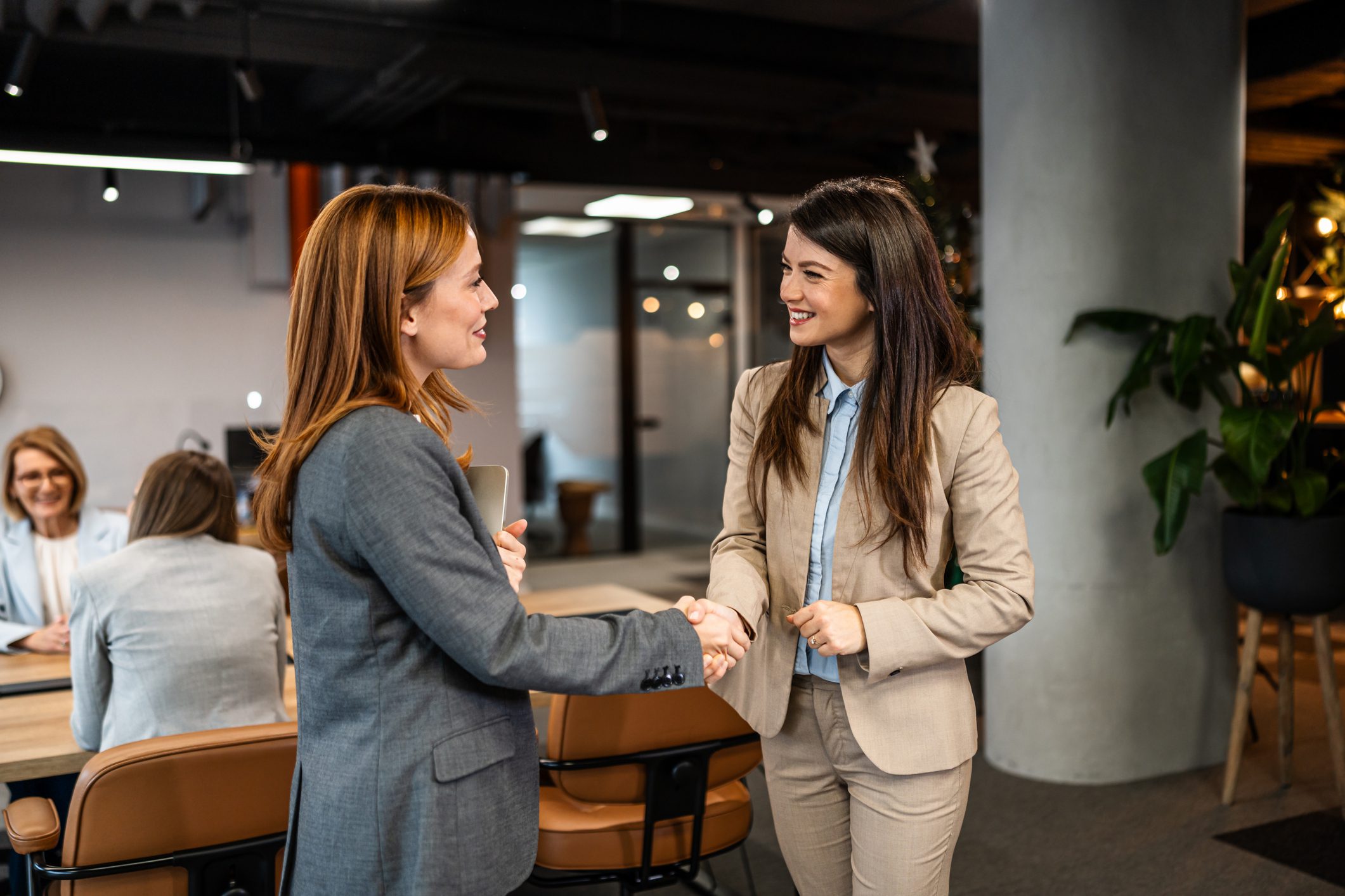 Two businesswomen concluding a deal with a handshake, demonstrating partnership and agreement in a professional office setting